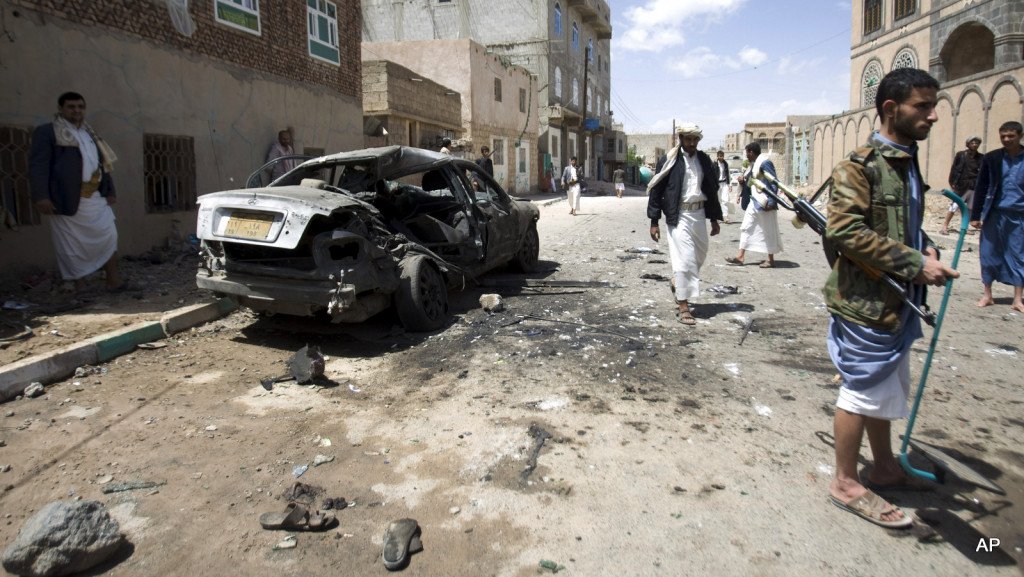 Shiite rebels, known as Houthis, stand near a damaged car after a bomb attack in Sanaa, Yemen, Friday, March 20, 2015. Triple suicide bombers hit a pair of mosques crowded with worshippers in the Yemeni capital, Sanaa, on Friday, causing heavy casualties, according to witnesses. The attackers targeted mosques frequented by Shiite rebels, who have controlled the capital since September. (AP Photo/Hani Mohammed)