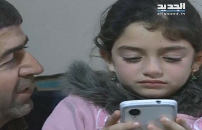 An image grab from an Al-Jadeed report shows Marianna Mazeh playing on a phone next to her uncle in their south Lebanon village of Tayr Filsey. (The Daily Star/Al-Jadeed, image grab)