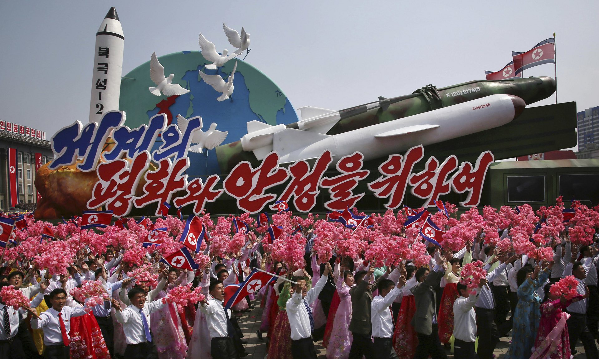 North Koreans wave national flags and artificial flowers while marching alongside a float carrying models of different missiles. Photograph: Wong Maye-E/AP