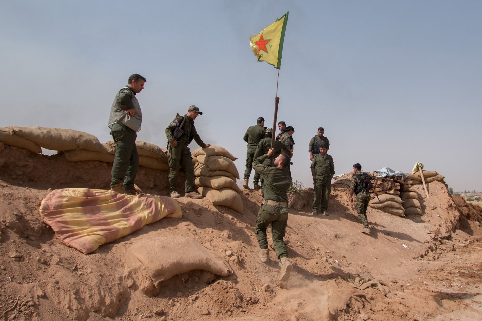 A YPG fighter raises a YPG flag over a barrier in Tel al-Aghbish village, which they retook control of from IS. Source: Reuters